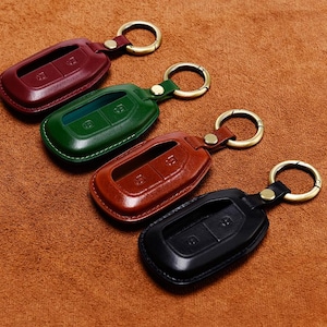 Puede incluir: Cuatro fundas de llavero de cuero en burdeos, verde, marrón y negro. Cada funda tiene un llavero y un botón para la entrada sin llave. Los llaveros están sobre una superficie de cuero marrón.
