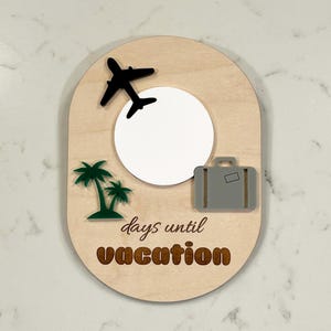 May include: A wooden countdown plaque with a white circle in the center, a black airplane, a gray suitcase, and two green palm trees. The text "days until vacation" is written in brown letters.