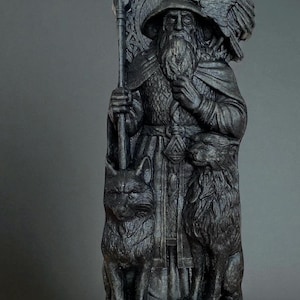 Peut inclure: Statue gris fonc&eacute; d'un homme barbu portant un chapeau et une cape, tenant un b&acirc;ton. Un aigle est perch&eacute; sur son &eacute;paule, avec un loup et un renard &agrave; ses pieds. La statue pr&eacute;sente des d&eacute;tails complexes.