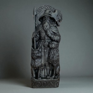 Peut inclure: Une statue gris fonc&eacute; d'Odin, une figure avec une longue barbe, un chapeau et une lance. La statue repr&eacute;sente un corbeau, deux figures animales et le mot "ODIN" &agrave; la base. La statue pr&eacute;sente des d&eacute;tails complexes et un aspect vieilli.