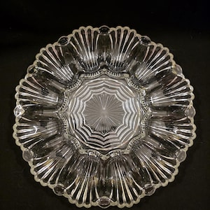 May include: A clear glass serving dish with a scalloped edge and a starburst design in the center. The dish has a circular shape with multiple sections, perfect for serving appetizers or snacks. The glass is transparent, allowing the contents to be visible.