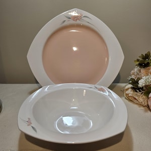 May include: Two-piece dinnerware set featuring a large, peach-colored plate and a white bowl. The plate has a unique, angular shape with a white border. Both pieces are decorated with a delicate floral design in pink and gray.