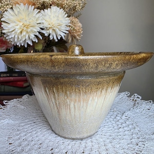 May include: A handcrafted ceramic vase with a unique design. The vase features a wide, shallow top and a conical base. The color transitions from a dark brown at the top to a creamy white at the bottom, with a dripped effect. The vase is likely for decorative purposes.