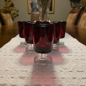 May include: A set of six small stemmed glasses featuring deep red bowls and clear glass bases. The glasses are arranged in a triangular formation, each with a cylindrical bowl shape, a short stem, and a circular foot, showcasing a consistent design.