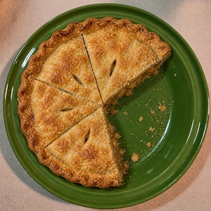 May include: A partially sliced apple pie on a green plate. The pie has a golden-brown crust with decorative edges and small slits. The plate is a solid, vibrant green.