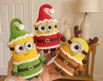 Peut inclure: Trois figurines faites à la main au crochet, de style Minion, en tenue de fête. L'une porte un chapeau et un costume de Père Noël rouge, une autre un chapeau et une tenue d'elfe verts, et la troisième a des bois de renne bruns et une tenue rayée.