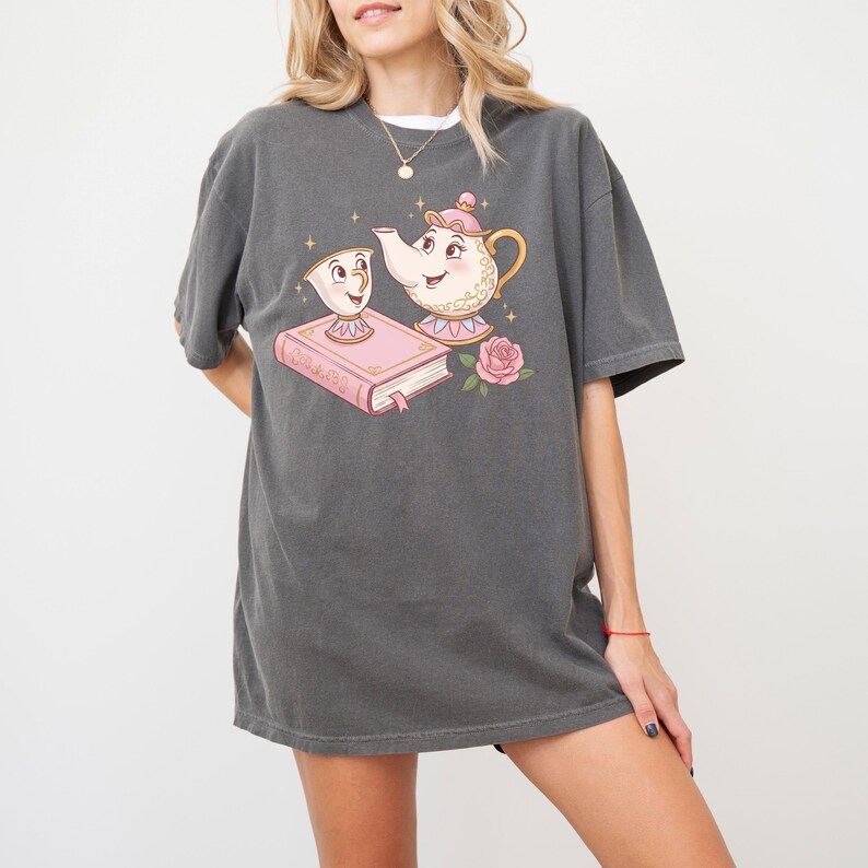 May include: A dark gray t-shirt with a graphic print of a teapot and a teacup from the Disney movie Beauty and the Beast. The teapot and teacup are holding a pink book with the text "Tale as Old as Time".