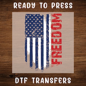 May include: A DTF transfer featuring a distressed American flag design with the word "FREEDOM" in red. The flag has blue stars and stripes in white and red. The text "READY TO PRESS" and "DTF TRANSFERS" are at the top and bottom.