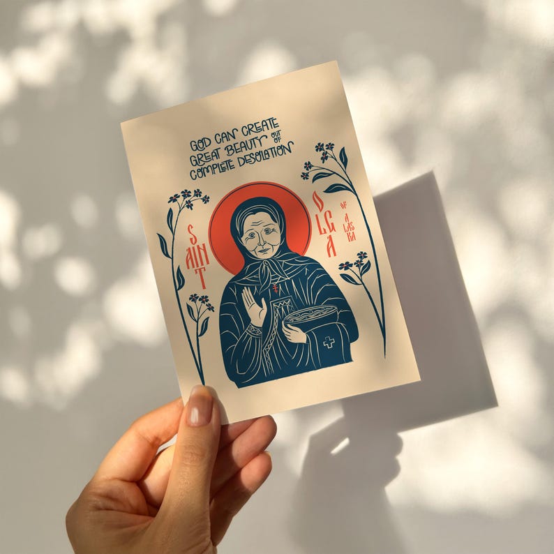 Puede incluir: Una tarjeta de felicitaci&oacute;n rectangular con una ilustraci&oacute;n estilizada de Santa Olga de Alaska en tinta azul oscuro sobre un fondo crema. El texto dice: GOD CAN CREATE GREAT BEAUTY OUT OF COMPLETE DESOLATION. Un halo rojo rodea la cabeza.