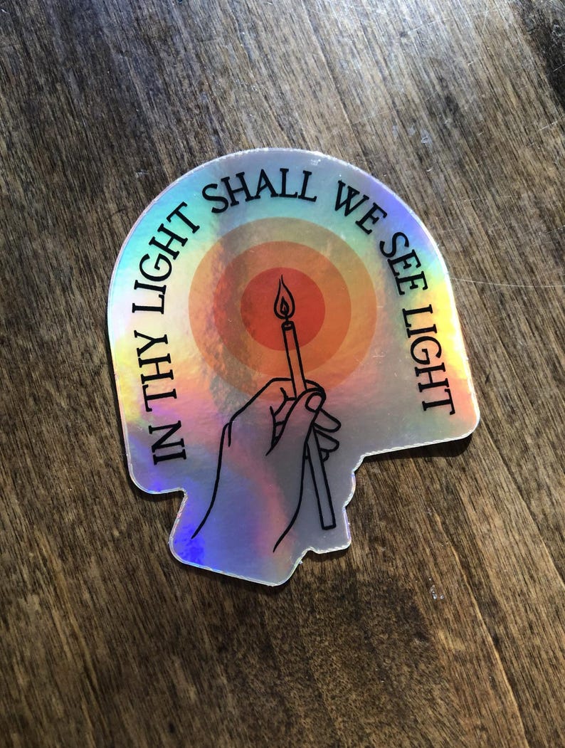 Puede incluir: Pegatina hologr&aacute;fica con el texto "IN THY LIGHT SHALL WE SEE LIGHT" en semic&iacute;rculo. La pegatina presenta una mano sosteniendo una vela encendida sobre un fondo de arco&iacute;ris.