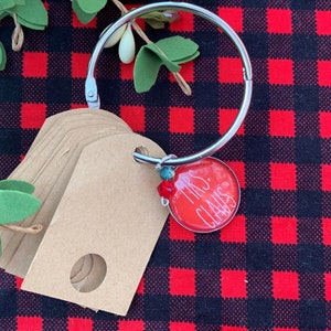 May include: A silver ring with a red round tag that says "Mrs. Claus" and a stack of brown gift tags with holes.