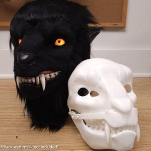 May include: A black wolf mask with glowing orange eyes and sharp white teeth is displayed next to a white mask with similar features. The black mask has a furry texture, while the white mask appears to be made of plastic. The text at the bottom says "Black wolf mask not included".