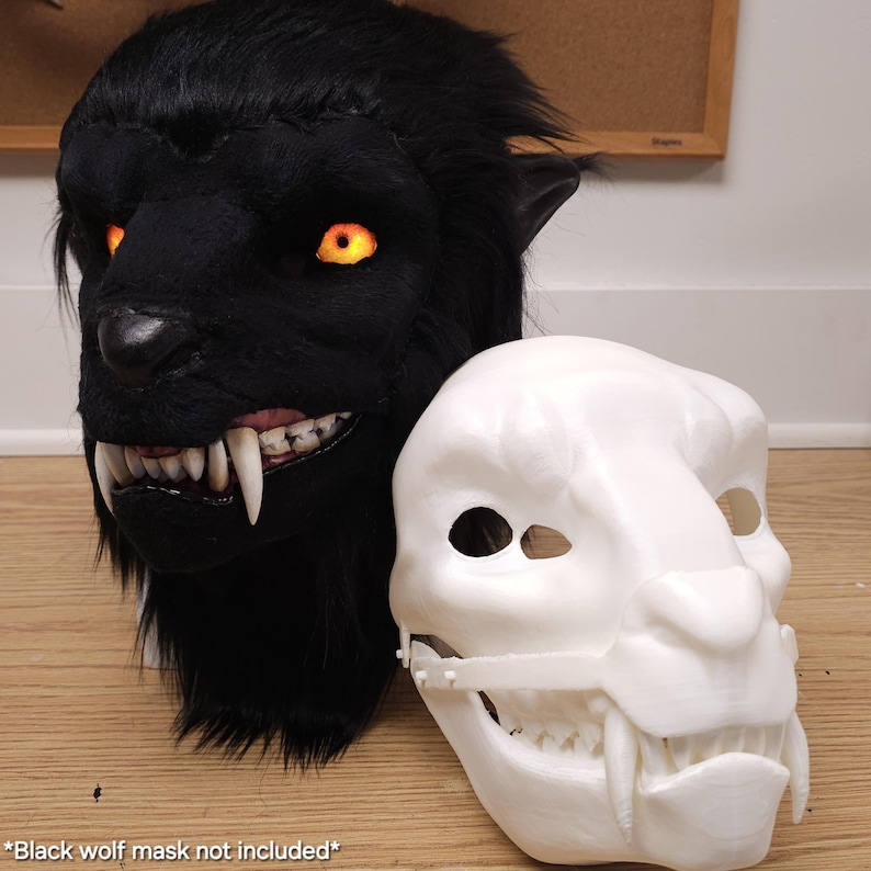 May include: A black wolf mask with glowing orange eyes and sharp white teeth is displayed next to a white mask with similar features. The black mask has a furry texture, while the white mask appears to be made of plastic. The text at the bottom says "Black wolf mask not included".