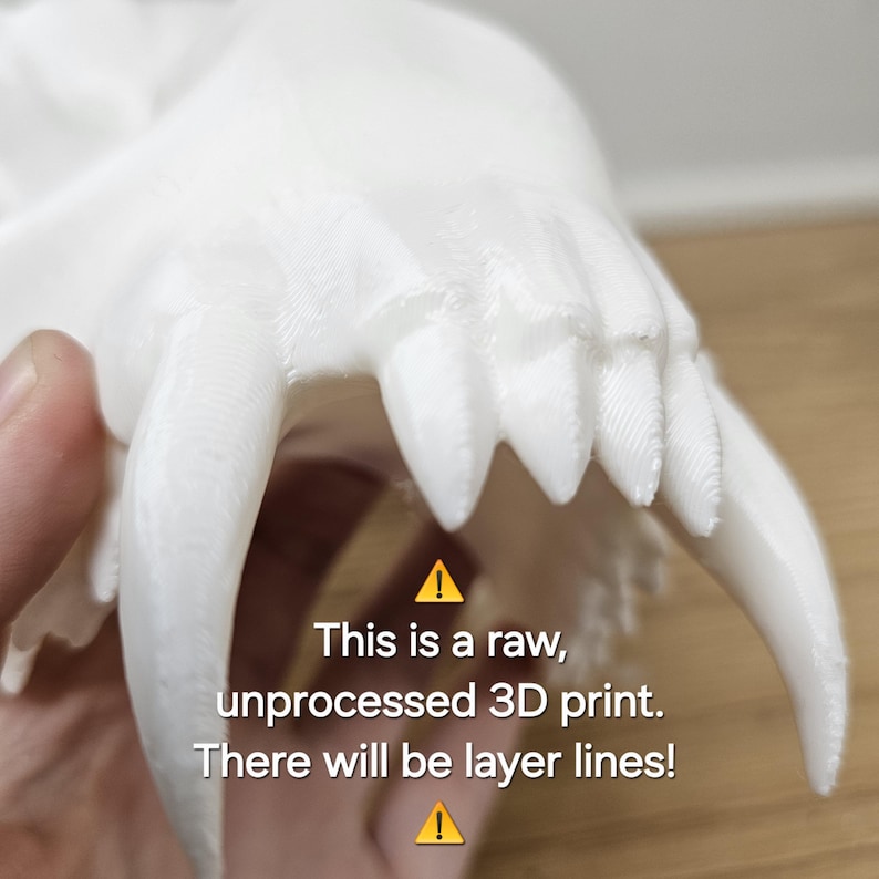 May include: A white 3D-printed model of a skull, featuring prominent fangs and detailed texture. The text on the image reads: "This is a raw, unprocessed 3D print. There will be layer lines!"