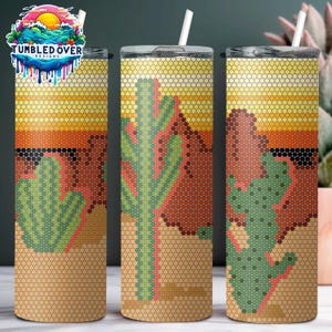 Puede incluir: Tres vasos cilíndricos con pajitas blancas, con un diseño de paisaje desértico compuesto por un patrón de rejilla hexagonal. El estampado muestra cactus verdes, formaciones rocosas rojas y un cielo de atardecer amarillo, con el logo Tumbled Over Designs.