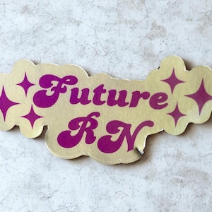 May include: A gold-coloured, cloud-shaped sticker with the words "Future RN" in a retro font. The text is in a vibrant purple colour, and there are purple starburst accents around the edges.