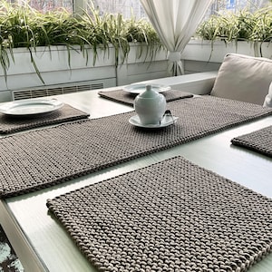 May include: Four brown knitted placemats on a white table with a white ceramic sugar bowl and a white saucer on one of the placemats.