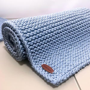 May include: A light blue knitted blanket with a brown leather tag that says "Hand Made".