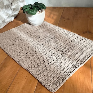 May include: A beige crocheted rug with a diamond pattern. The rug is laid out on a wooden floor.