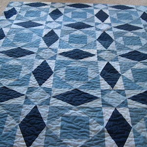 May include: A quilt made from blue denim fabric in various shades. The quilt is made up of a repeating pattern of diamonds and squares.