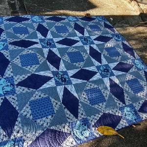 May include: A blue and white quilt with a star pattern. The quilt is made of different fabrics with various blue shades and white accents. The quilt is laid out on a concrete surface.