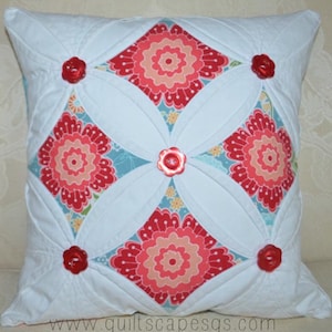 May include: A white pillow with a quilted design featuring red and pink floral patterns. The pillow has four large red buttons.