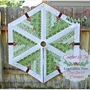 May include: A white, green, and red quilted Christmas tree skirt with a log cabin design. The skirt has a black and white trim and a red ribbon tie. The text "Comfort & Joy Log Cabin Tree Tree Skirt & Ornaments" is printed on a white background.