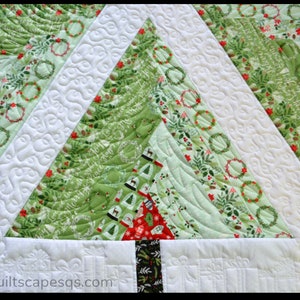 May include: A green and white Christmas quilt with a quilted tree design. The tree is made of different fabrics with a variety of Christmas patterns, including wreaths, holly, and snowflakes. The quilt is quilted with a swirling pattern.