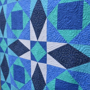May include: A quilt with a star pattern in shades of blue, teal, and white. The quilt is made of different fabrics with various patterns.
