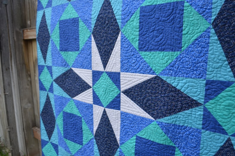 May include: A quilt with a star pattern in shades of blue, teal, and white. The quilt is made of different fabrics with various patterns.