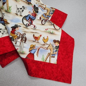 May include: A white fabric with a red border features a repeating pattern of children playing on a farm. The children are wearing cowboy hats and riding tricycles, horses, and rocking horses. There are also chickens and dogs in the pattern.