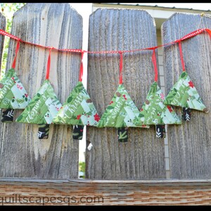 May include: A Christmas tree garland with red ribbon and green fabric trees with the words "Merry Christmas" and "Happy New Year" on them.