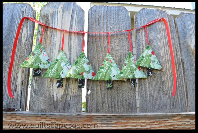 May include: A Christmas tree garland with red ribbon and green fabric trees with the words "Merry Christmas" and "Happy New Year" on them.