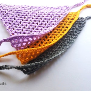 May include: Three handmade crochet bandanas in shades of purple, gold, and gray. Each bandana features a triangular shape with a crocheted open weave design and long ties for securing around the neck. The bandanas are displayed on a white surface.