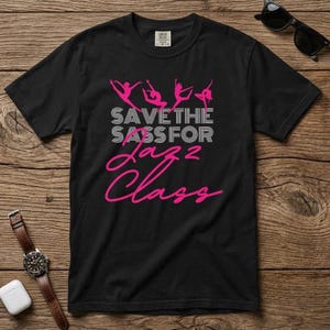 May include: Black t-shirt with a pink graphic of dancing figures and the text "SAVE THE SASS FOR Jazz Class". The shirt is made of a soft material and is suitable for casual wear.