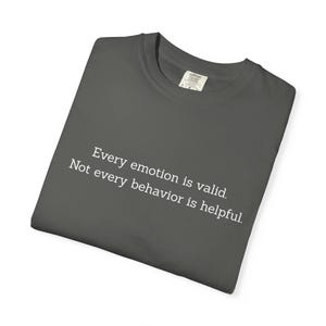 Peut inclure: T-shirt gris foncé avec le texte "Every emotion is valid. Not every behavior is helpful." Le t-shirt a un col rond et une étiquette au dos. Le t-shirt est plié.