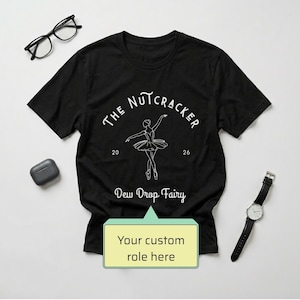 May include: A black short-sleeved t-shirt featuring a white line-art illustration of a ballerina. The text reads THE NUTCRACKER, 20 26, and Dew Drop Fairy. A light green speech bubble graphic at the bottom contains the text Your custom role here.