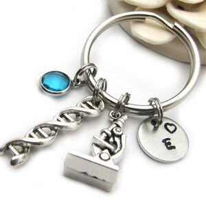 May include: Silver keychain with a blue crystal, a DNA double helix charm, a microscope charm, and a round charm with a heart and the letter E.