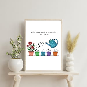 May include: A framed print with the text "WHAT YOU CHOOSE TO FOCUS ON...WILL GROW." It depicts a watering can pouring water onto five potted plants labeled "Love," "Worry," "Self-Doubt," "Guilt," and "Anxiety." The plants are in colorful pots.