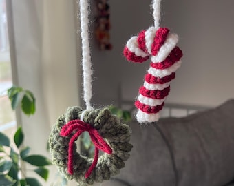 May include: Crocheted Christmas decorations. The image shows a green wreath with a red bow and a red and white striped candy cane, hanging from white yarn. These handmade ornaments are perfect for festive holiday decor.