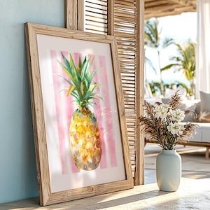 Peut inclure: Une impression encadrée à l'aquarelle d'un ananas. L'ananas est jaune et orange avec des feuilles vertes, sur un fond à rayures roses et blanches. Le cadre est en bois clair.