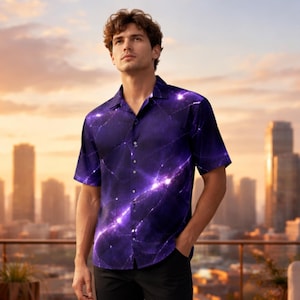 Op de afbeelding: Een overhemd met korte mouwen met een paars galaxy-ontwerp, gecombineerd met een zwarte broek en witte sneakers. Het patroon van het overhemd heeft heldere witte en paarse strepen. De persoon staat op een terras met een skyline op de achtergrond.