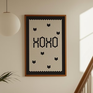 May include: A framed wall art piece with a mosaic design. The artwork features the letters "XOXO" in black, surrounded by black hearts on a white and black tile background. The frame is brown.