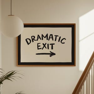May include: A rectangular wall art piece in a light wood frame featuring a cream-colored background with a thick black border. The text DRAMATIC EXIT is printed in bold black capital letters, accompanied by a black arrow pointing to the right.