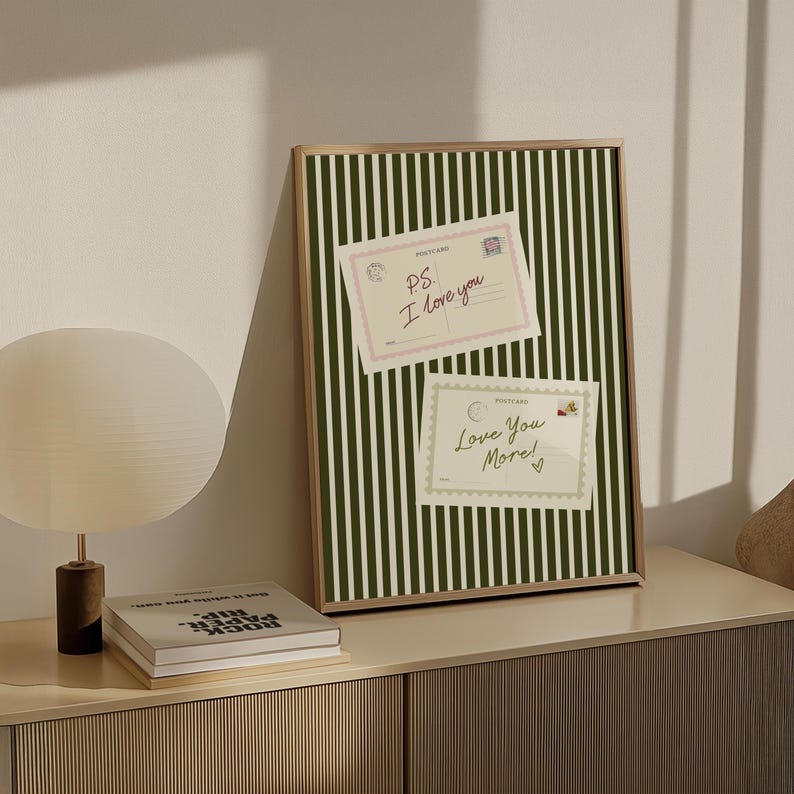 May include: A framed print with a green and white striped background. Two postcards are attached to the frame. The top postcard reads "PS. I love you" and the bottom postcard reads "Love You More!"