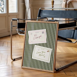 May include: A framed bulletin board with a green and white striped pattern. Two postcards are pinned to the board. The top postcard reads "PS I love you" and the bottom postcard reads "Love You More!"