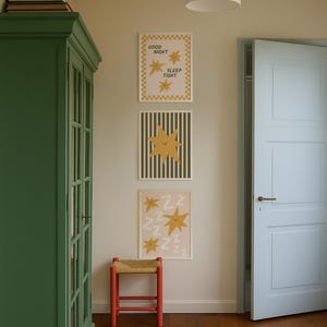 Puede incluir: Tres l&aacute;minas enmarcadas con dise&ntilde;os de estrellas cuelgan de una pared. Una l&aacute;mina dice "GOOD NIGHT SLEEP TIGHT". Un taburete rojo con asiento tejido est&aacute; debajo. Tambi&eacute;n se ven un armario verde y una puerta azul claro.