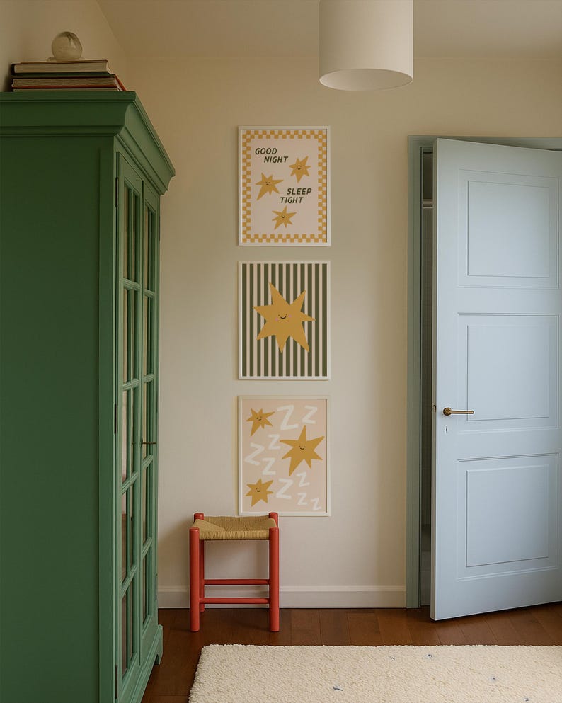Puede incluir: Tres l&aacute;minas enmarcadas con dise&ntilde;os de estrellas cuelgan de una pared. Una l&aacute;mina dice "GOOD NIGHT SLEEP TIGHT". Un taburete rojo con asiento tejido est&aacute; debajo. Tambi&eacute;n se ven un armario verde y una puerta azul claro.