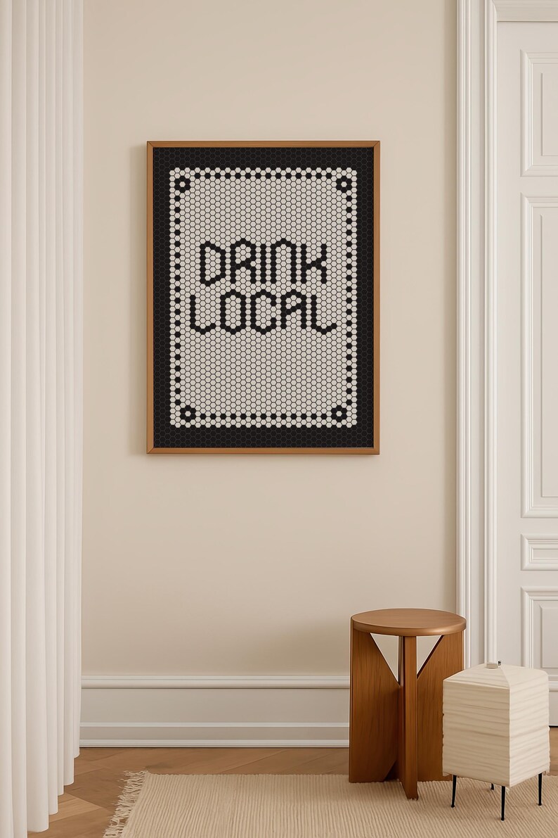 May include: A framed artwork with the words "DRINK LOCAL" in black letters. The text is set against a white background, surrounded by a black border, and framed in wood. The artwork is displayed on a beige wall.