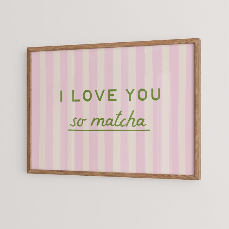 May include: A framed print with a pink and white striped background. The text "I LOVE YOU so matcha" is written in green. The frame is made of light brown wood.